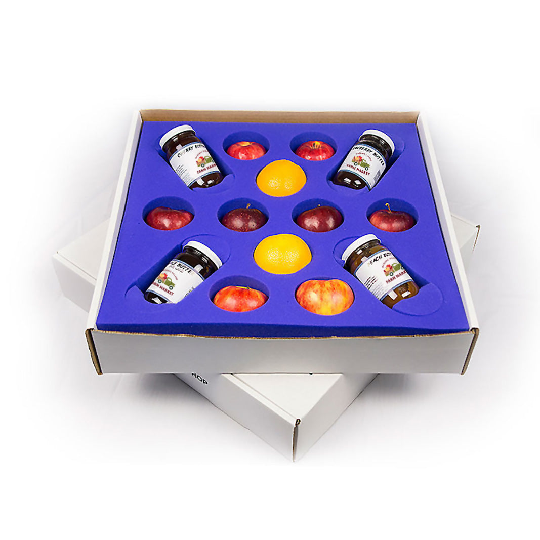 Box with compartments containing small jars, apples and oranges on a white background.