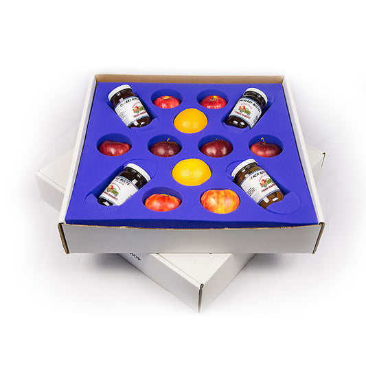 Box with compartments containing small jars, apples and oranges on a white background.