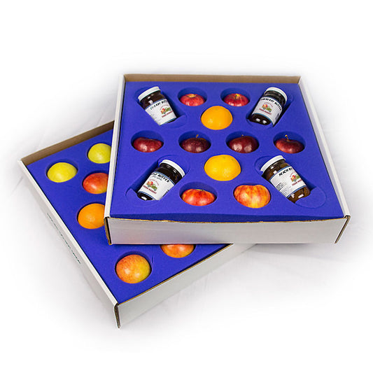 Two white boxes with blue foam interior compartments containing small jars, apples and oranges on a white background.