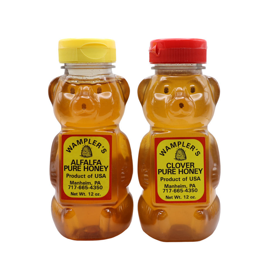 Two bear-shaped honey bottles with yellow and red lids on a white background
