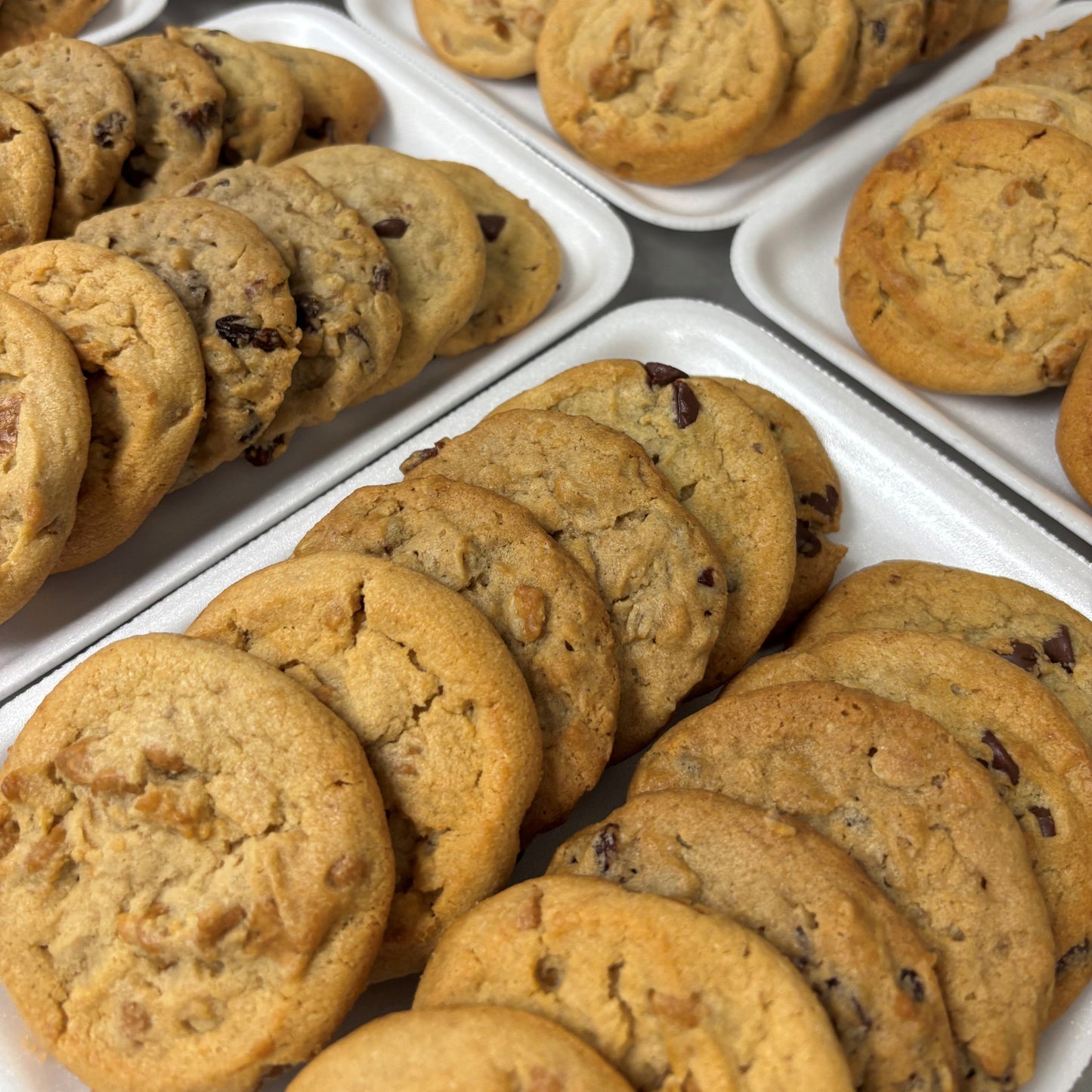 Multiple trays of chocolate chip cookies on a white surface.